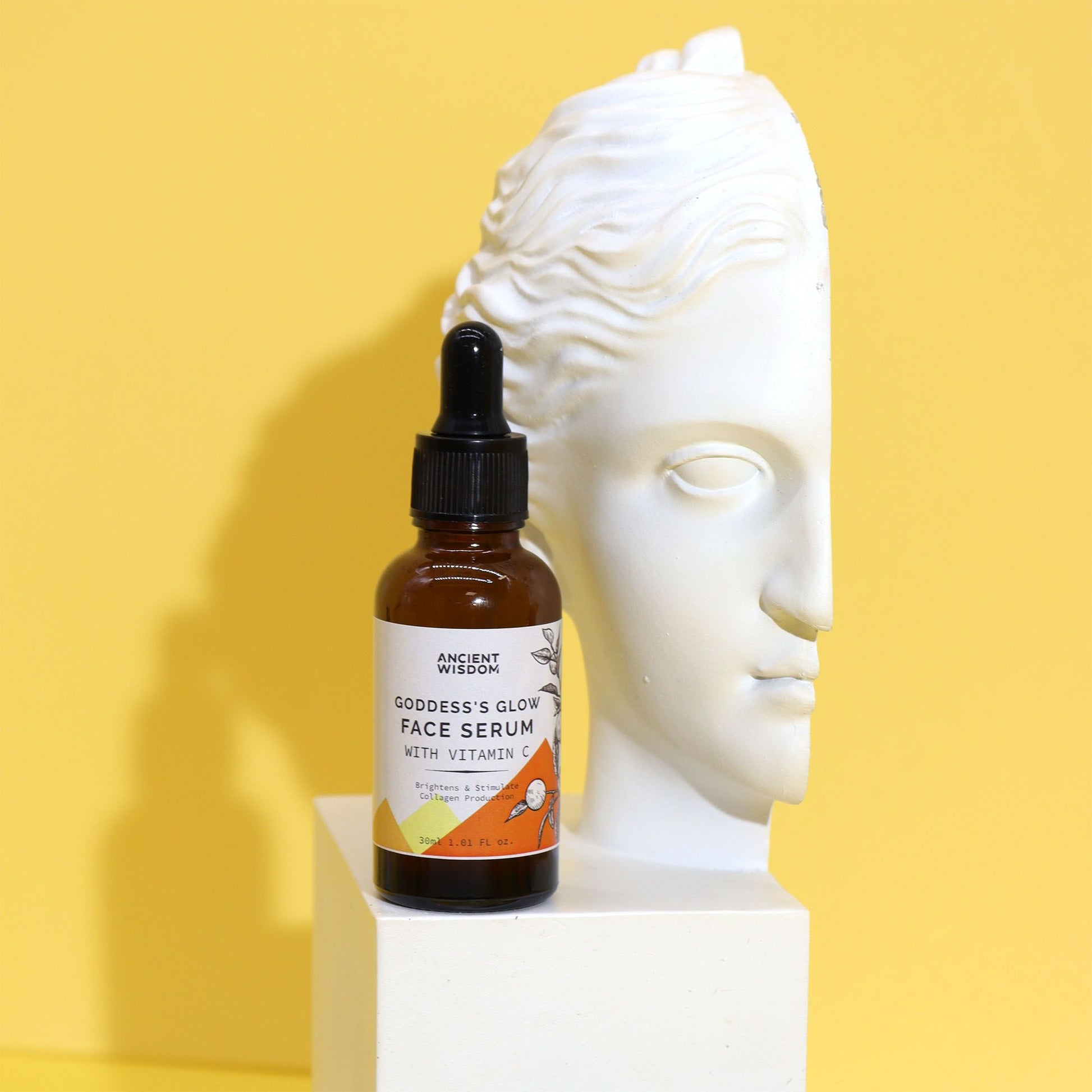 Frasco ámbar con cuentagotas de Sérum Facial Vitamina C Brillo Total junto a un busto blanco sobre fondo amarillo.
